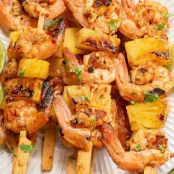 Grilled shrimp and pineapple skewers garnished with cilantro on a white plate.