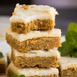 A stack of four frosted cookie bars with crumbs scattered around, garnished with a fresh mint sprig.