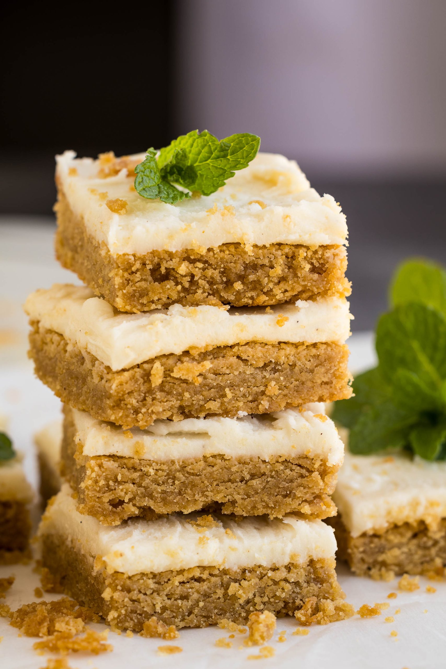 Four stacked square peanut butter graham cracker blondies with crumbly layers and cream-colored frosting, garnished with a mint leaf.