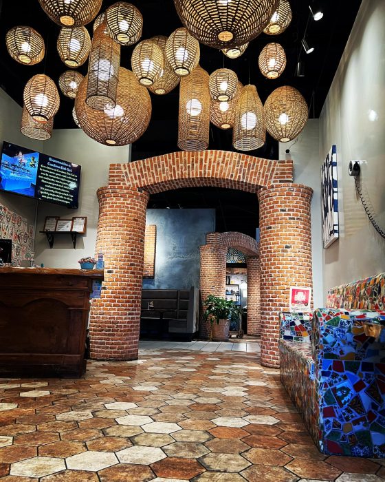 Interior of Cantina Del Solwith brick arches, tile flooring, and various hanging lights. A wooden counter is on the left, and mosaic seating is on the right. Television and plants are visible.